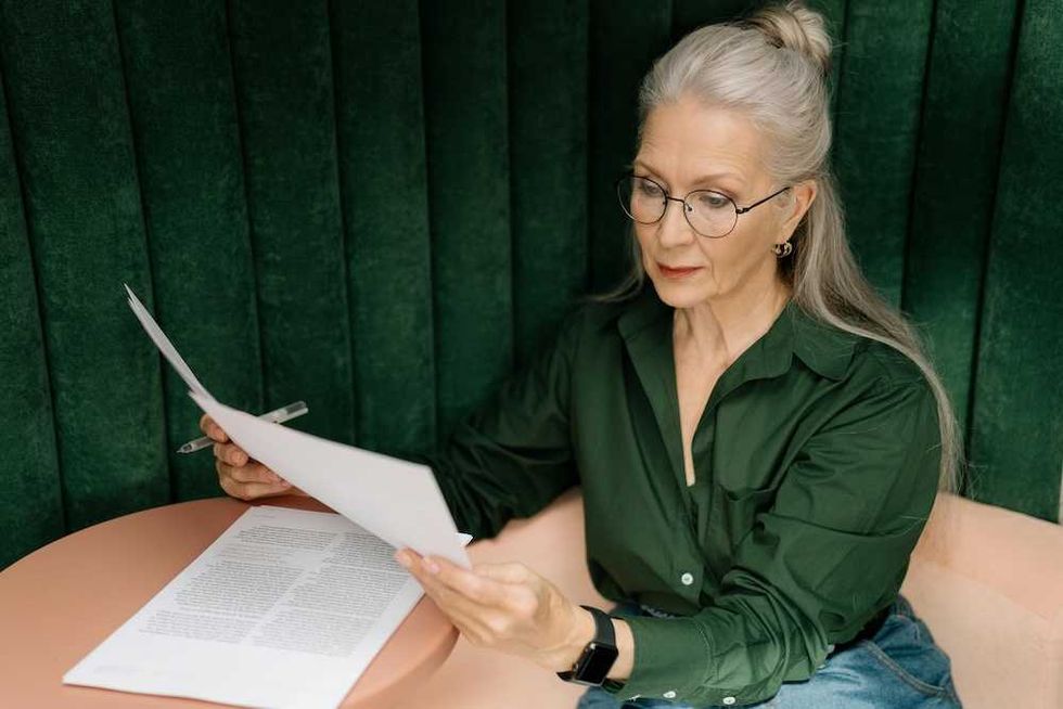 Woman in green shirt reading documents at a pink table.