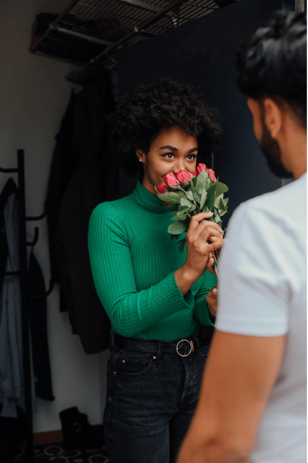 Woman in green sweater smiling at man with a bouquet of roses.