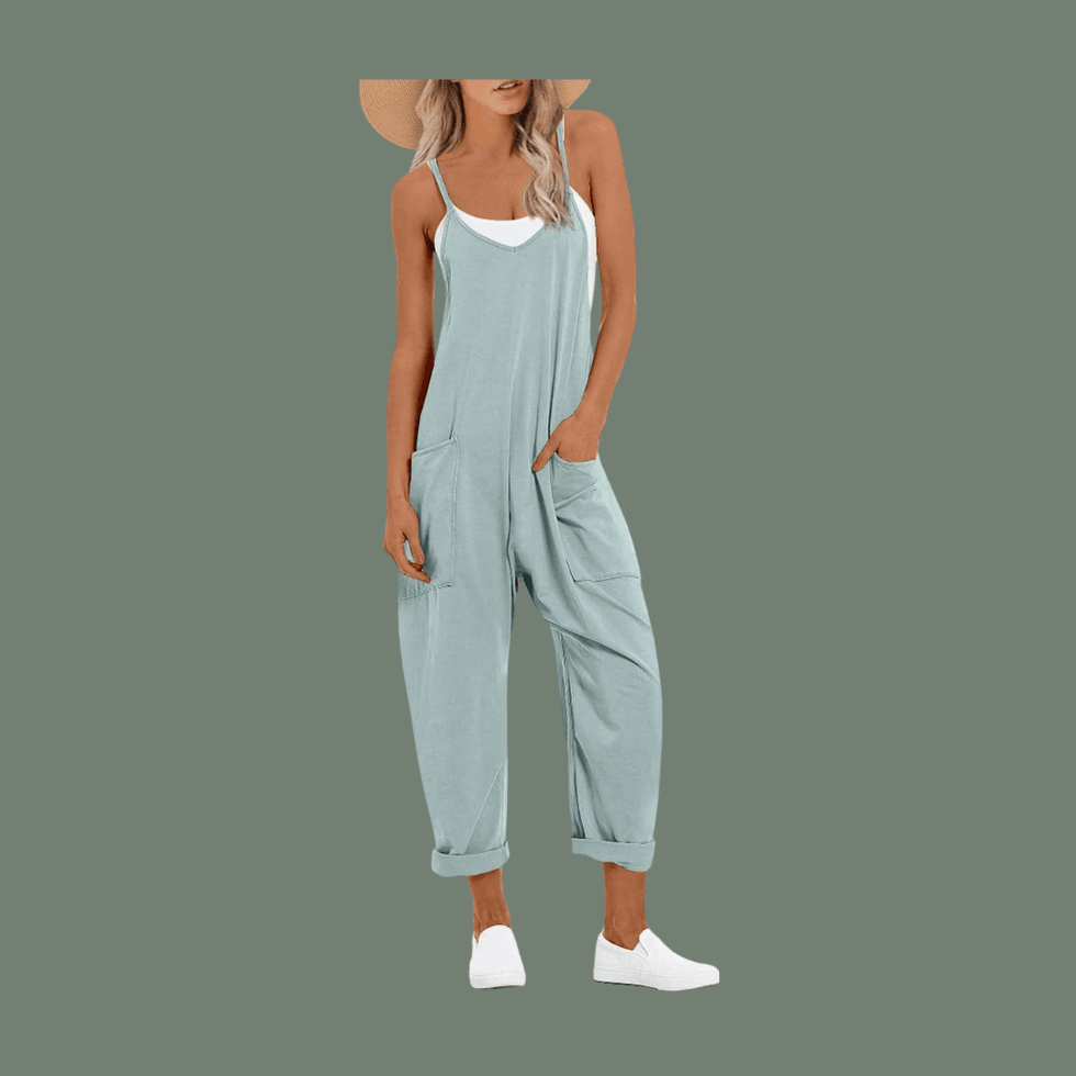 Woman in light blue overalls, white top, and sneakers on gray background.