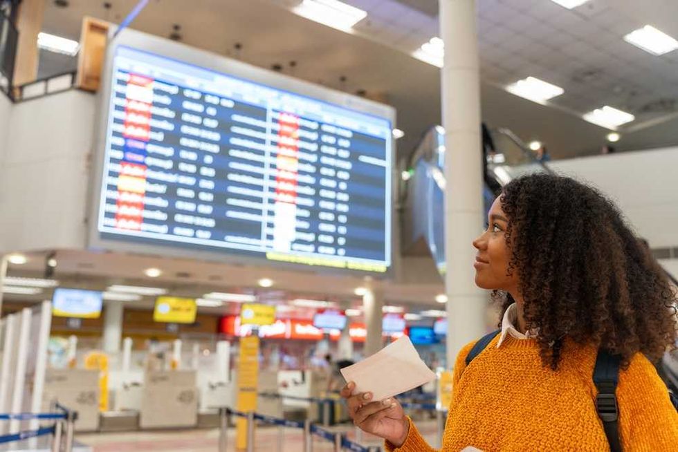 Woman in orange sweater checking flight information at an airport.