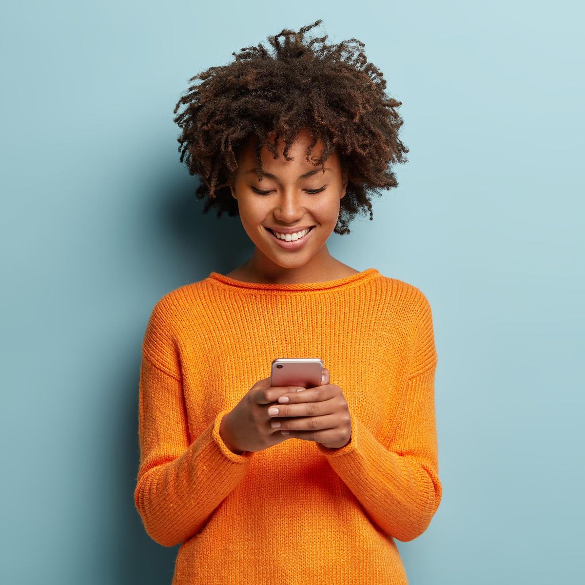 woman in orange sweater scrolling on smartphone