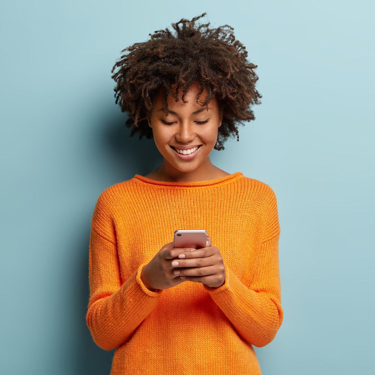 woman in orange sweater scrolling on smartphone 