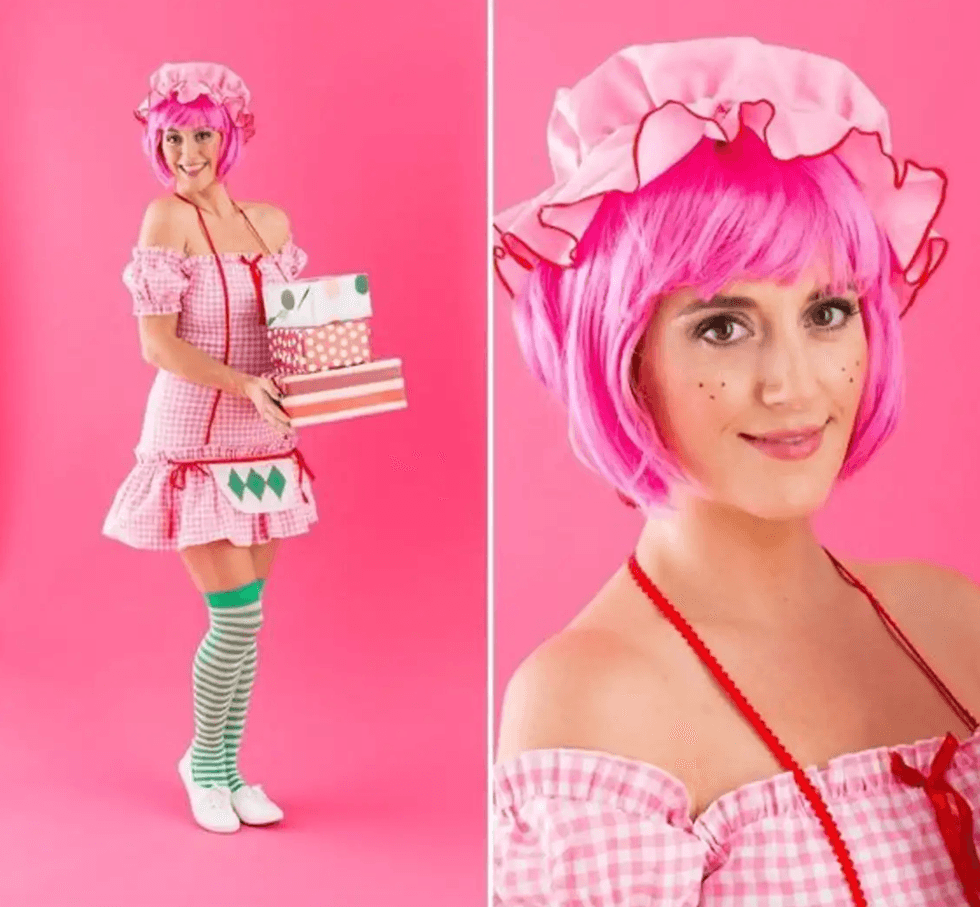 Woman in pink costume with wig, holding gift boxes against pink background.