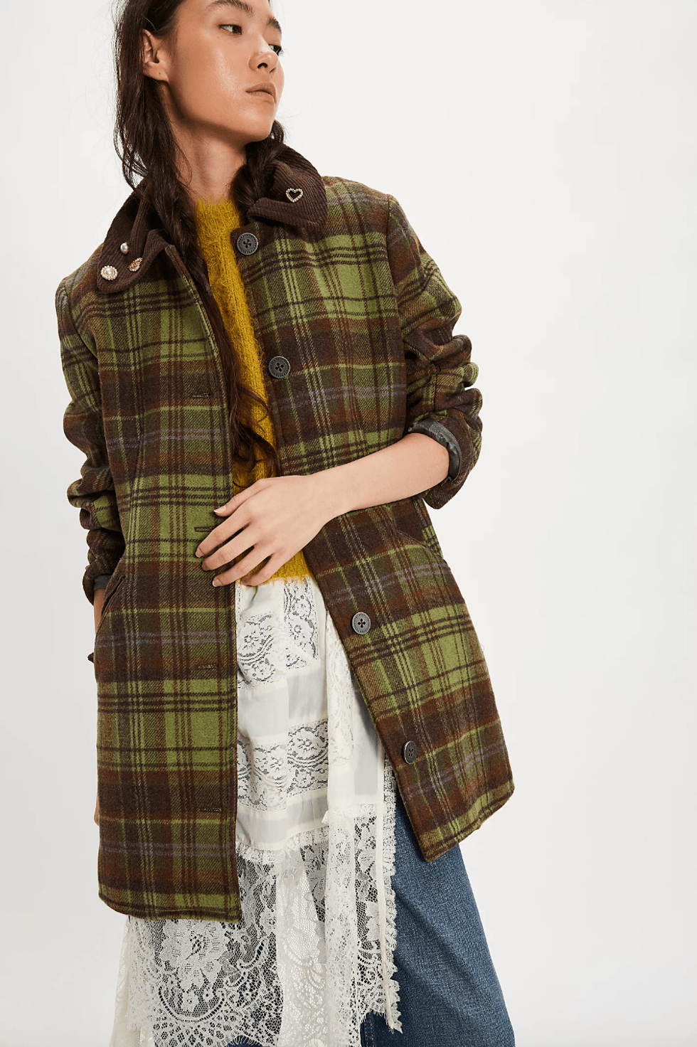 Woman in plaid coat with lace skirt and jeans, looking to the side.