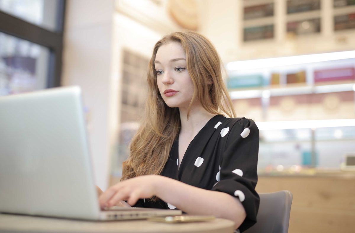 Woman in polka dot dress using a laptop at a table indoors.