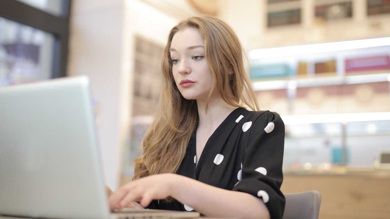 Woman in polka dot dress using a laptop at a table indoors.