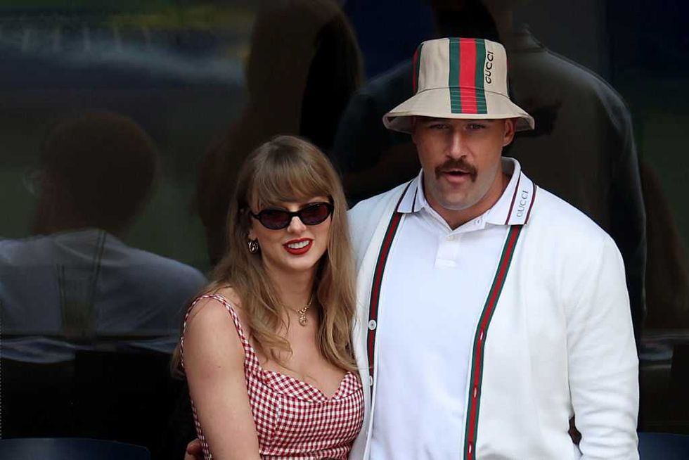 Woman in red dress and sunglasses with man in white outfit and hat at an event.