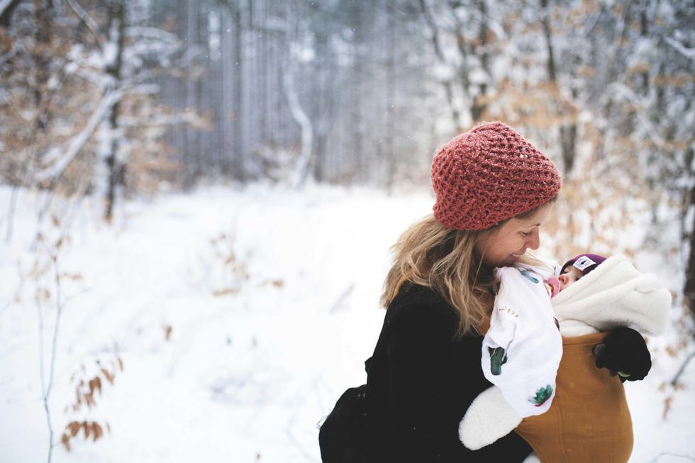 Woman in red hat holding baby in snowy forest.