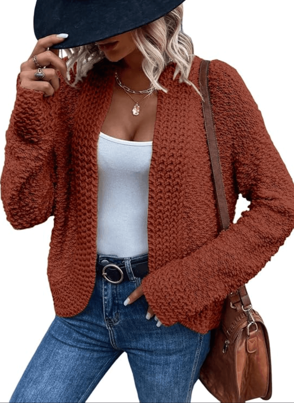 Woman in rust cardigan, white top, jeans, and black hat.