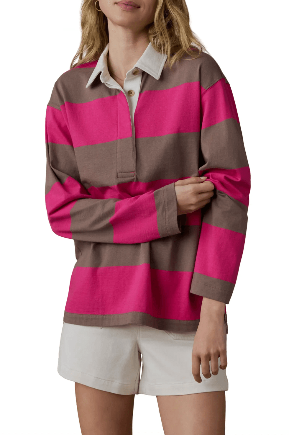 Woman in striped pink and brown rugby shirt with white shorts, arms crossed.
