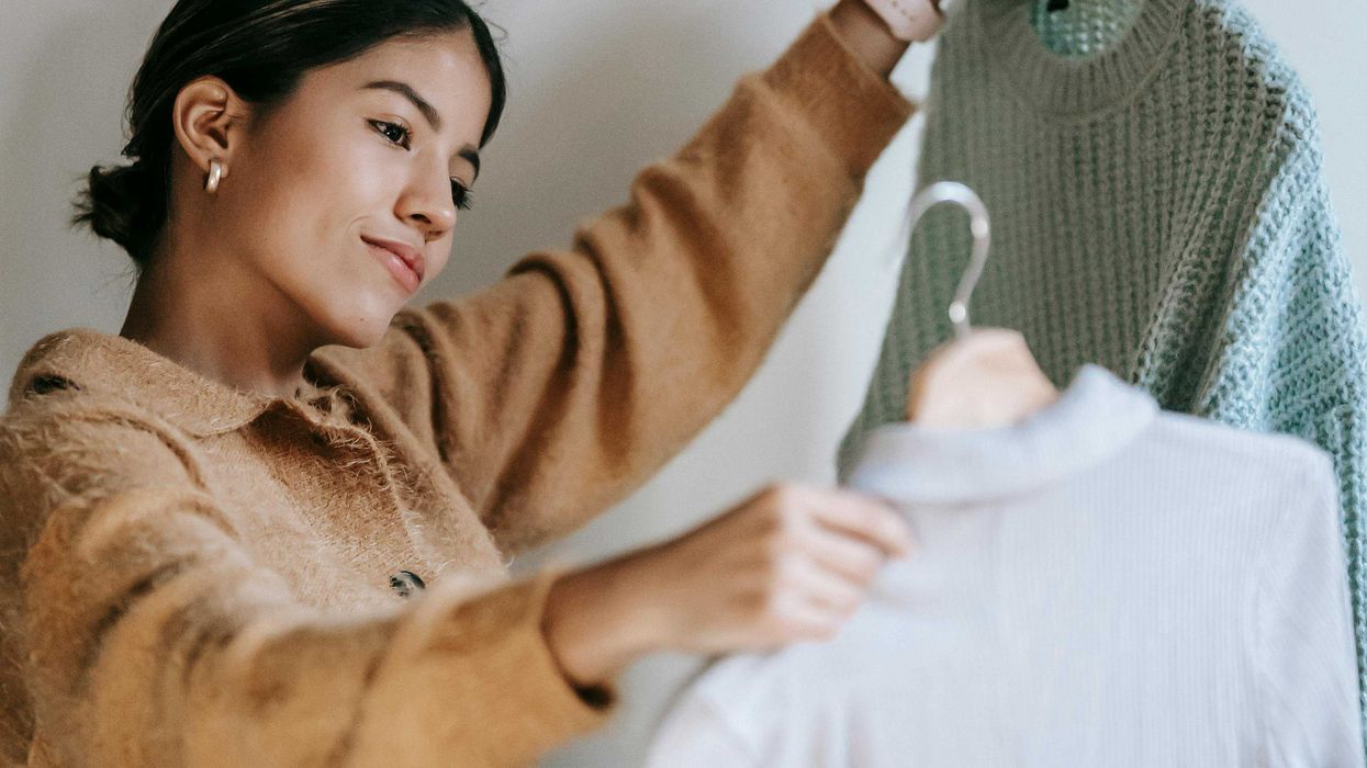 Woman in sweater holding two garments on hangers, deciding between them.