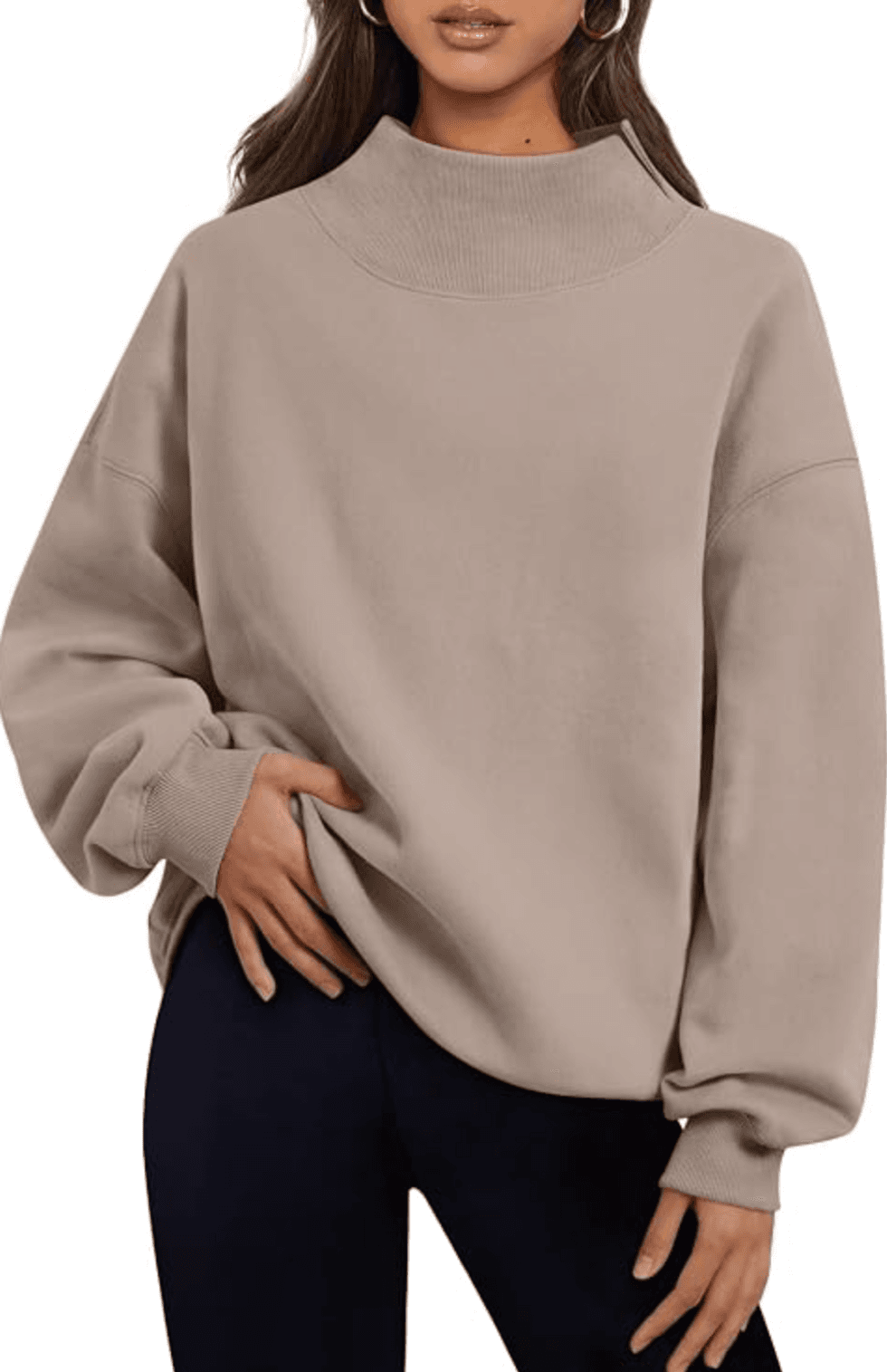 Woman in taupe turtleneck sweater and black pants, posing with hand on hip.