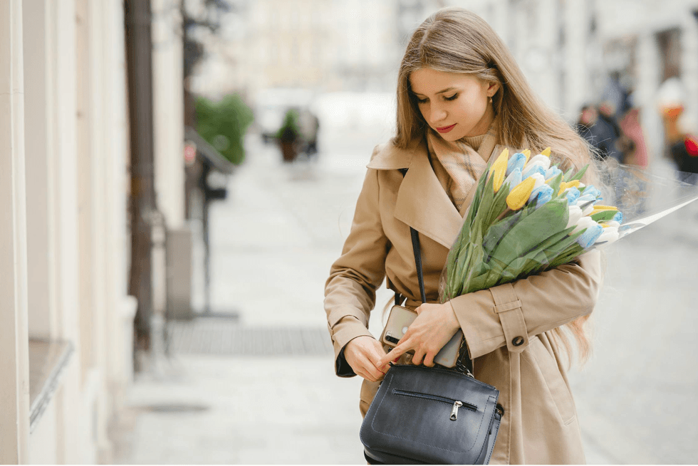 Woman in trench coat holding tulips, standing on a city street.