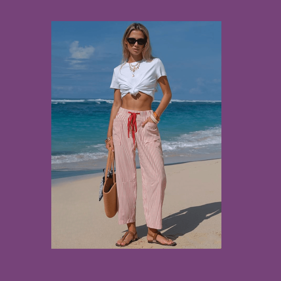 Woman in white crop top and striped pants standing on a sandy beach.