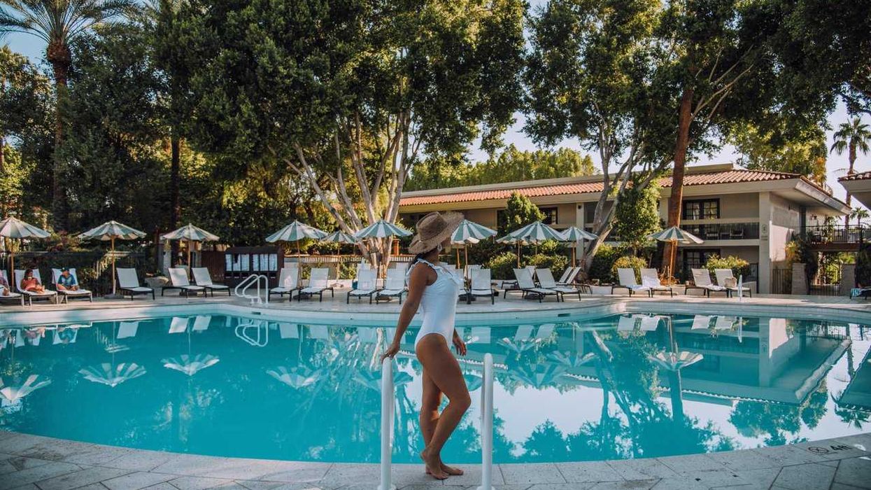Woman in white swimsuit stands by a tranquil pool with loungers and umbrellas in the background.