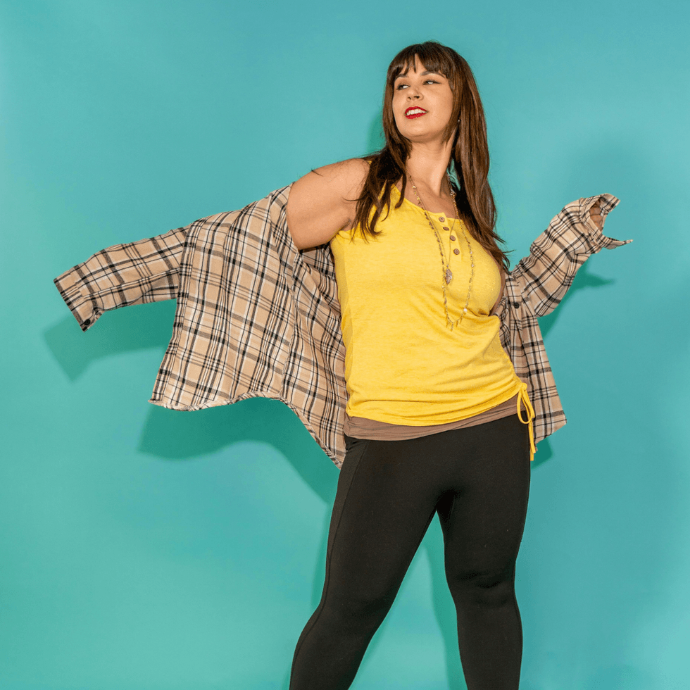 Woman in yellow top against a teal blue background wearing a plaid flannel shirt