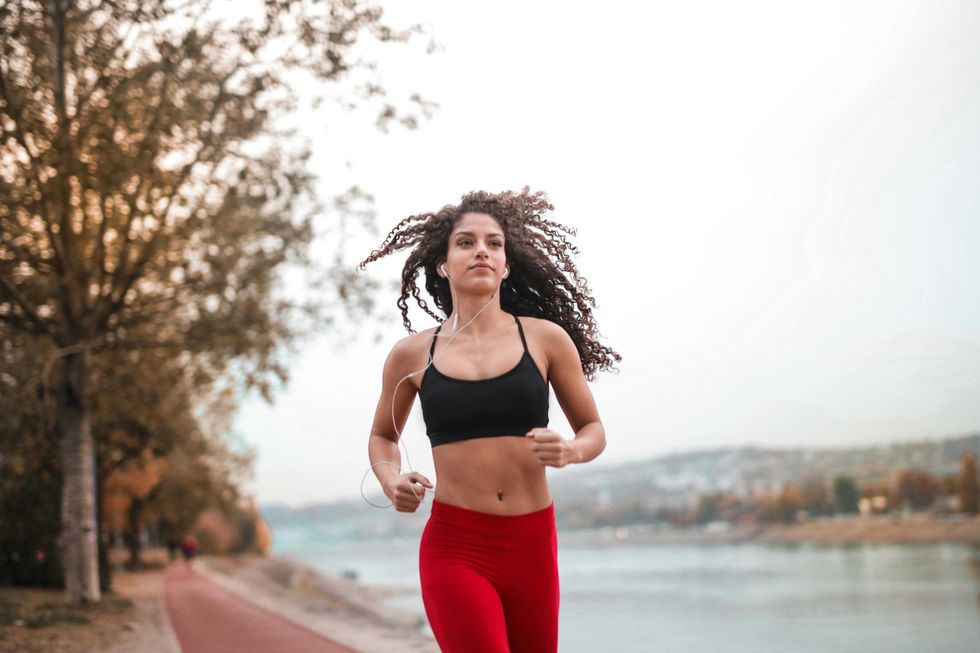 Woman jogging on a riverside path in red leggings and black top, with earphones.