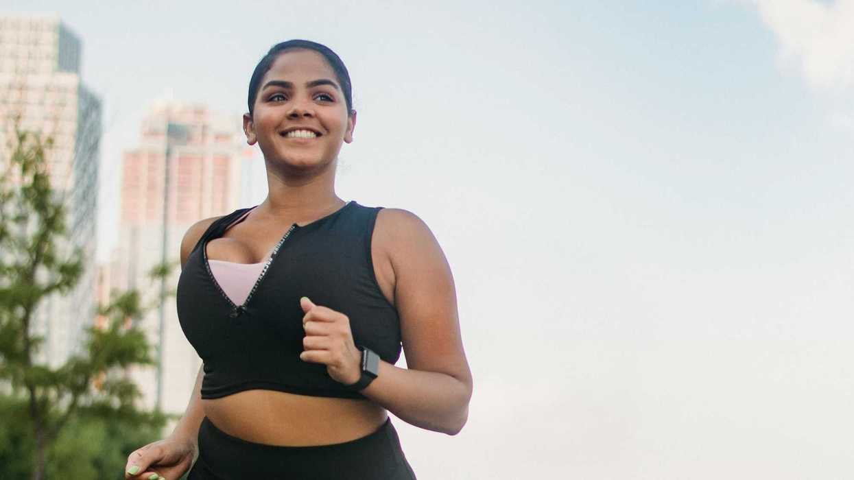 Woman jogging on a waterfront boardwalk, smiling under a clear sky.