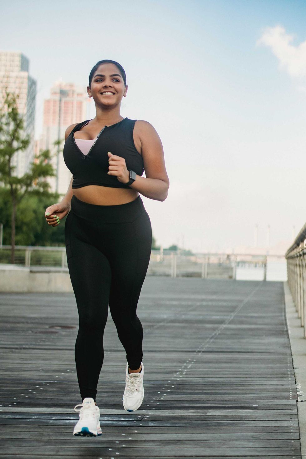 Woman jogging on a waterfront boardwalk, smiling under a clear sky.