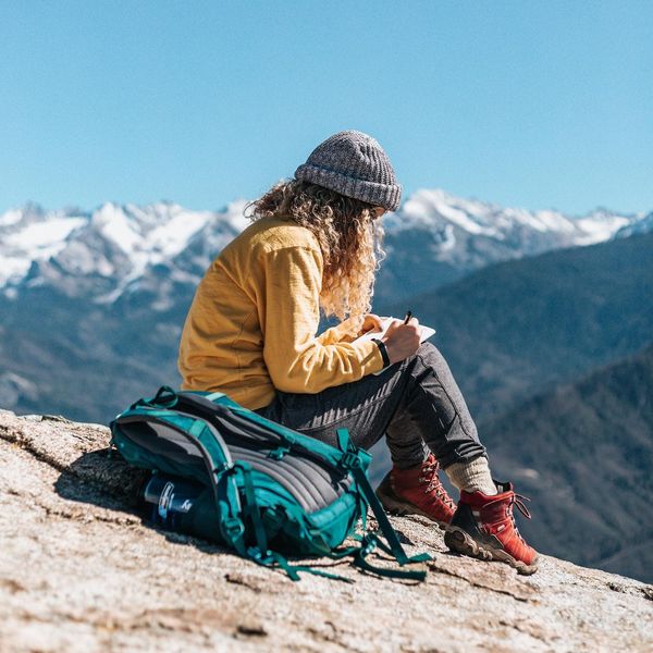 Woman journaling on a mountain hike with red boots, blue backpack, and yellow sweater features an off the grid digital detox travel destinations