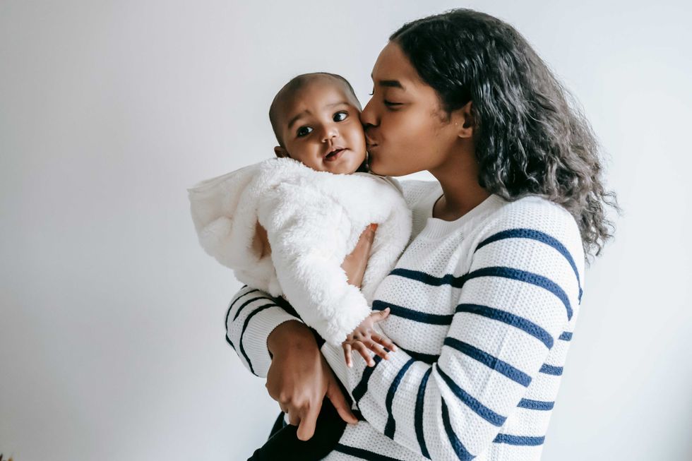 Woman kisses baby in white outfit, holding them close.
