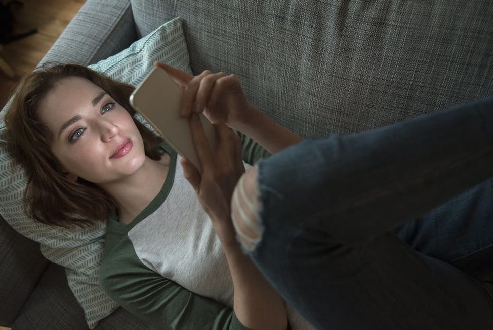 Woman laying on a couch in the dark while scrolling through her phone.