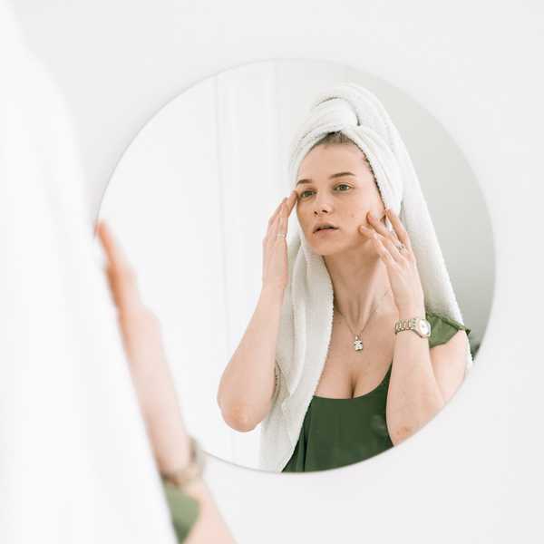 woman looking in the mirror, touching her face for lymphatic massage