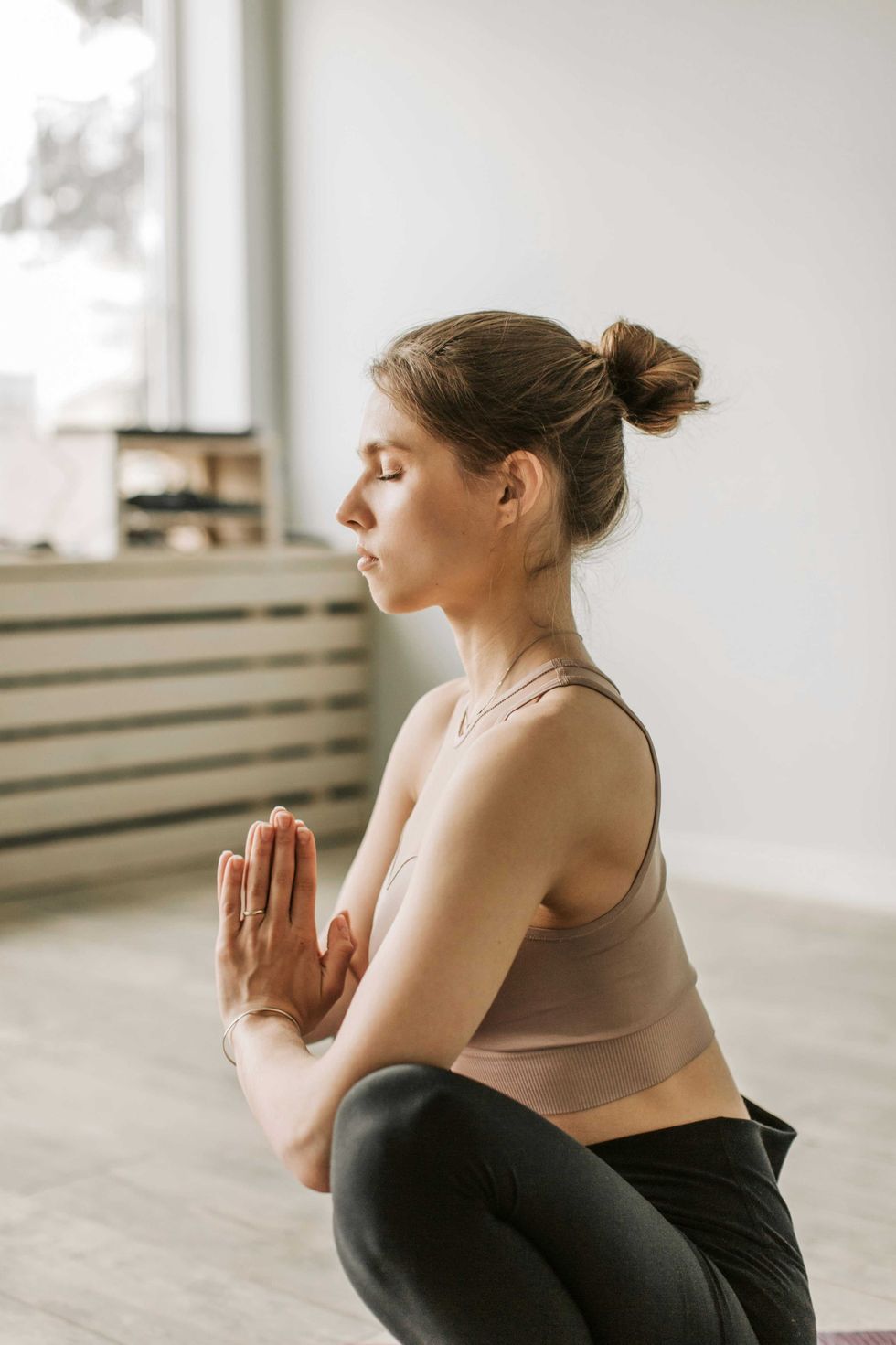 Woman meditating in a yoga pose with eyes closed, hands in prayer position.