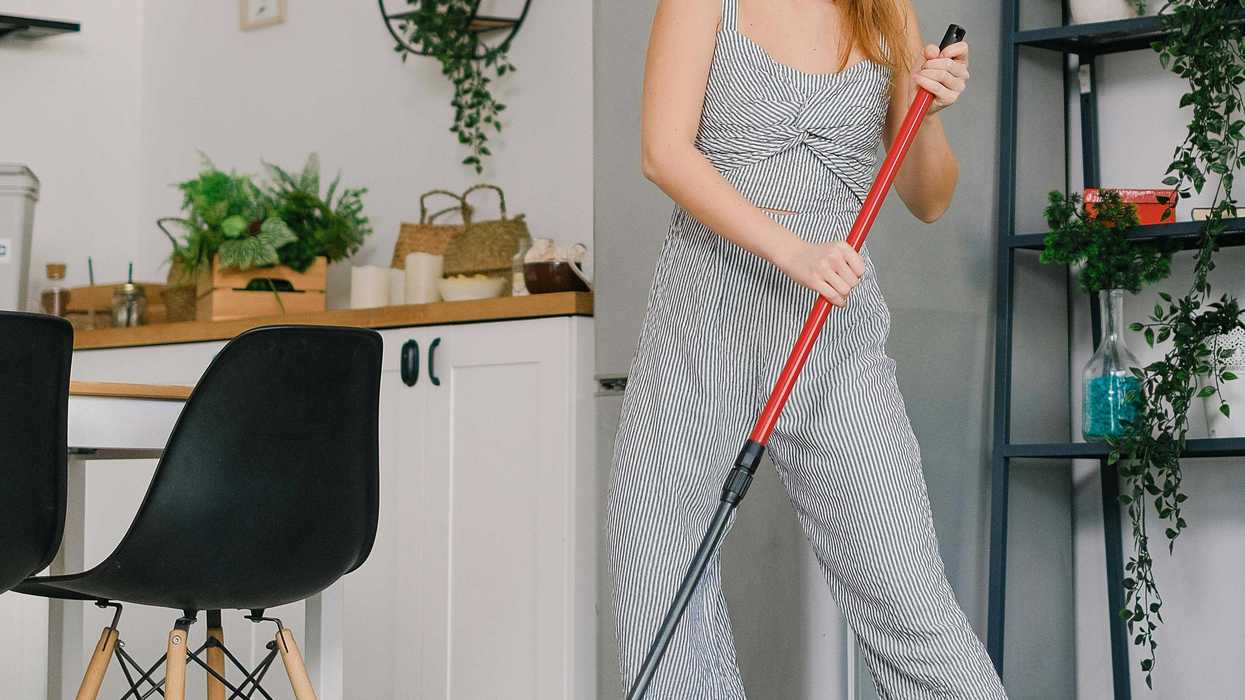 Woman mopping floor in a modern kitchen with plants and a yellow bucket nearby.