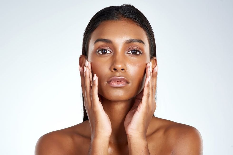 Woman of color touching her dewy complexion.