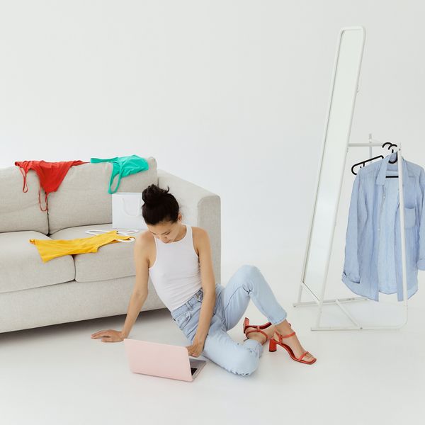 woman on her laptop with colorful clothes strewn on gray sofa