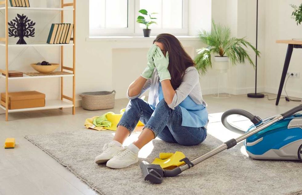 Woman overwhelmed by cleaning, sitting on floor with gloves and vacuum.