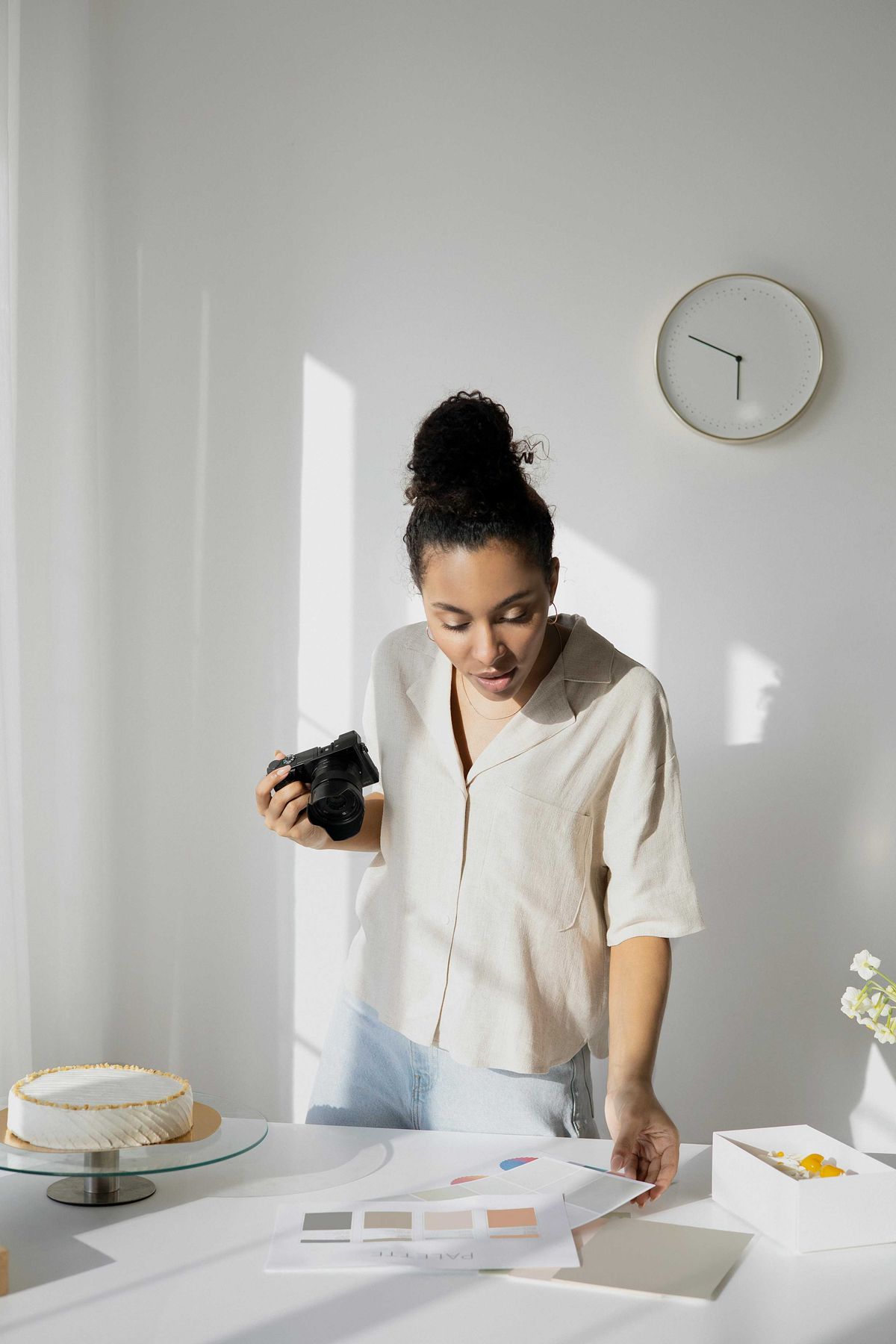 Woman photographing a cake on a table with color palettes and a wall clock.