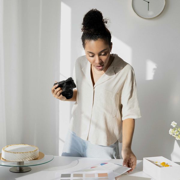 Woman photographing a cake on a table with color palettes and a wall clock.