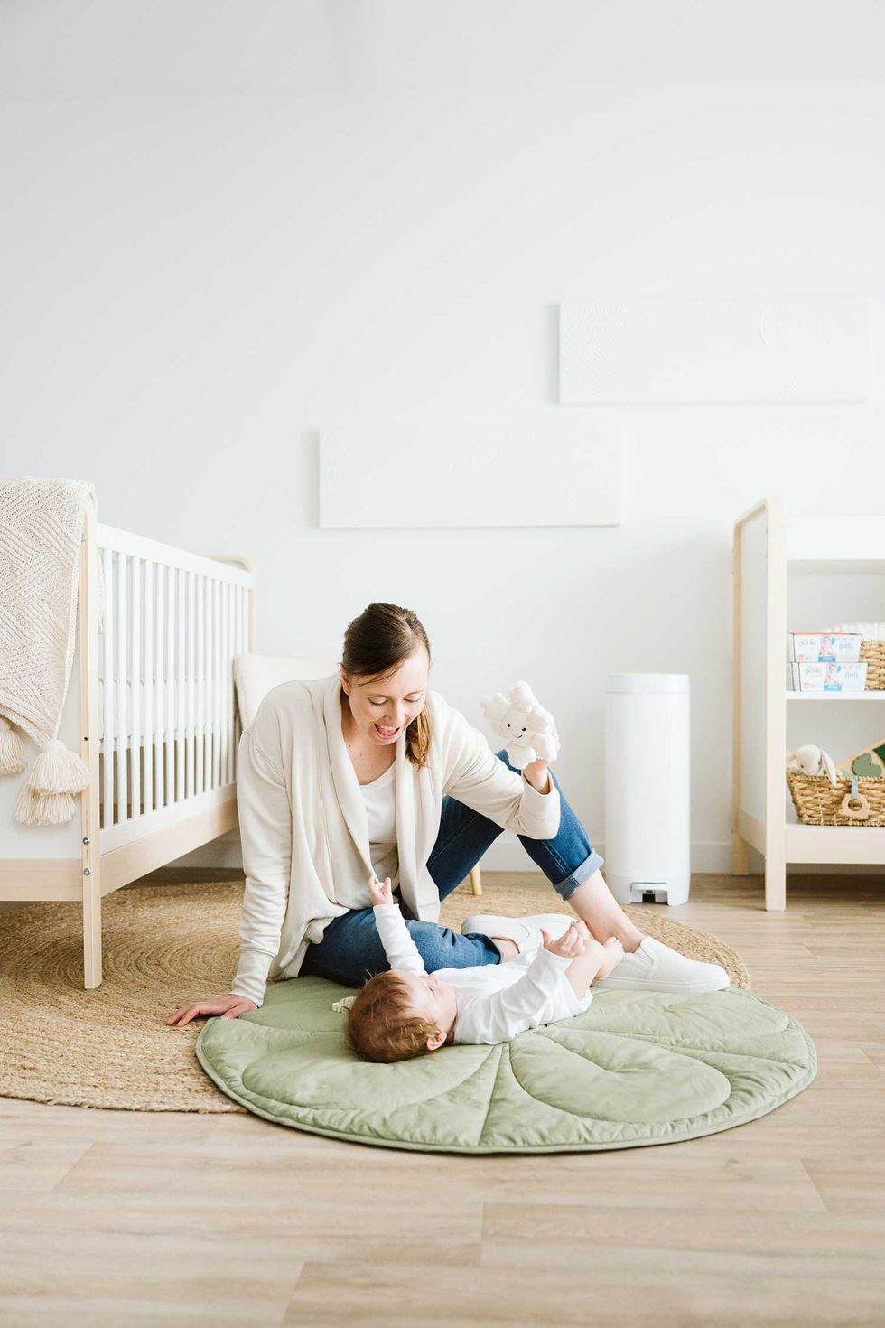 Woman playing with baby on a mat in a cozy, light nursery.