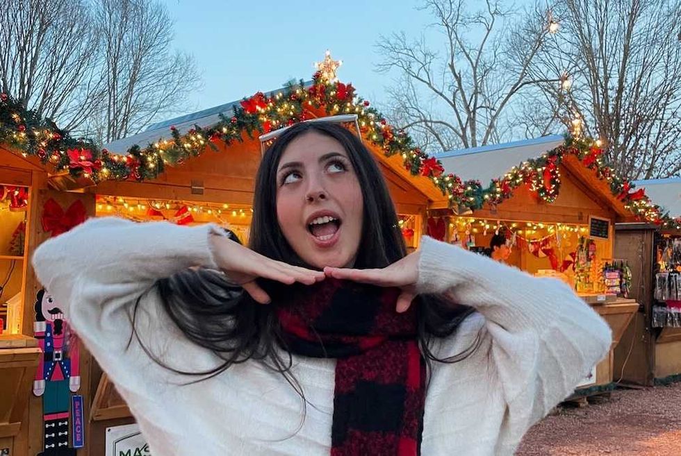 Woman posing cheerfully at a festive outdoor market with decorated stalls.