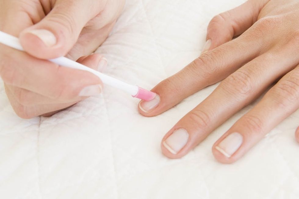 Woman pushing her cuticles back with a nail tool.