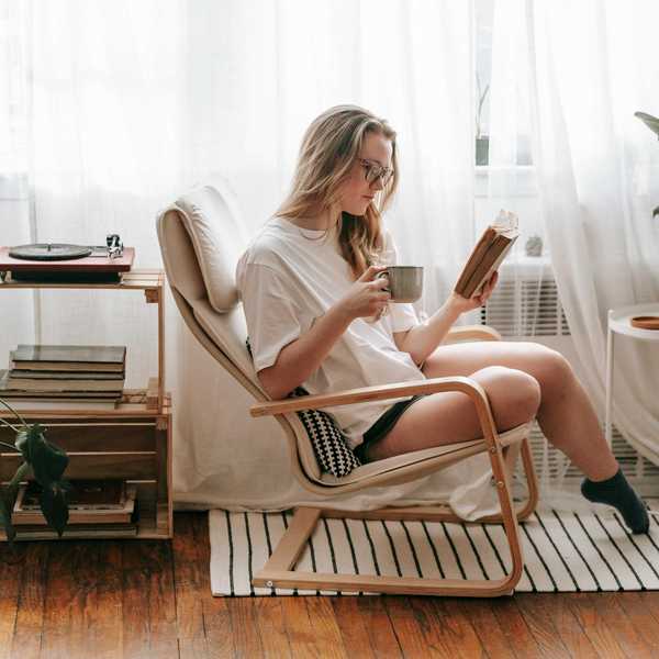 Woman reading a book with coffee in a cozy chair by a window.