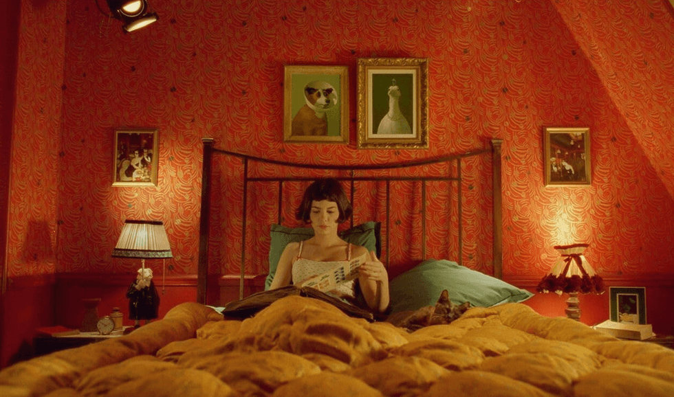Woman reading in bed with red wallpaper and eclectic art decor.
