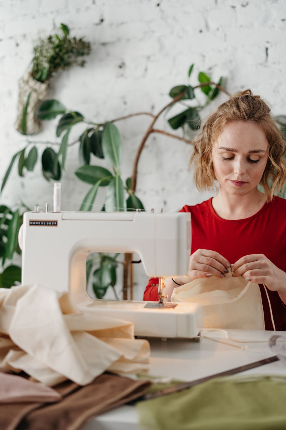 Woman sewing fabric with a sewing machine, surrounded by plants.