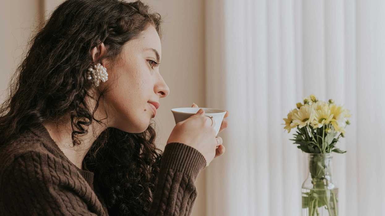 Woman sipping coffee by a book and flowers on a table.