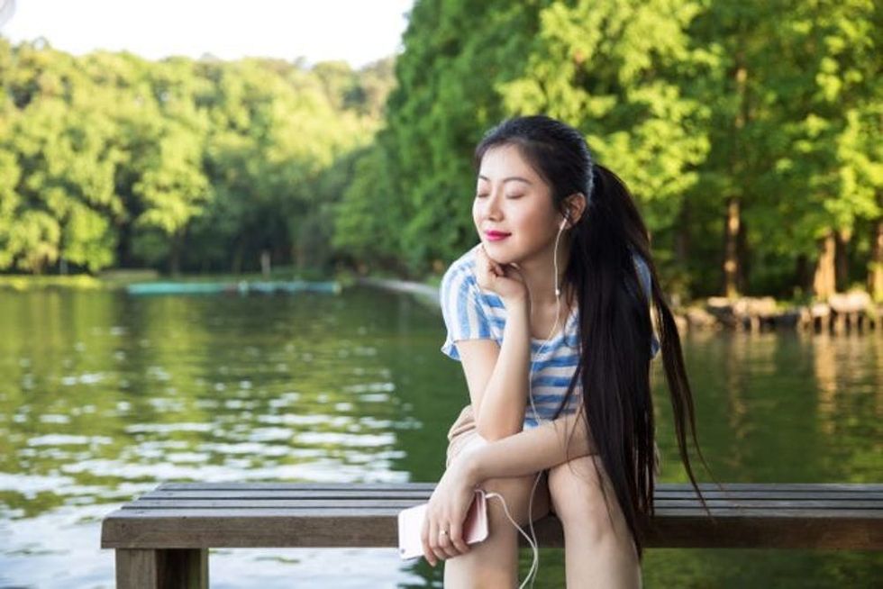 Woman sits on a pier listening to headphones plugged into her phone