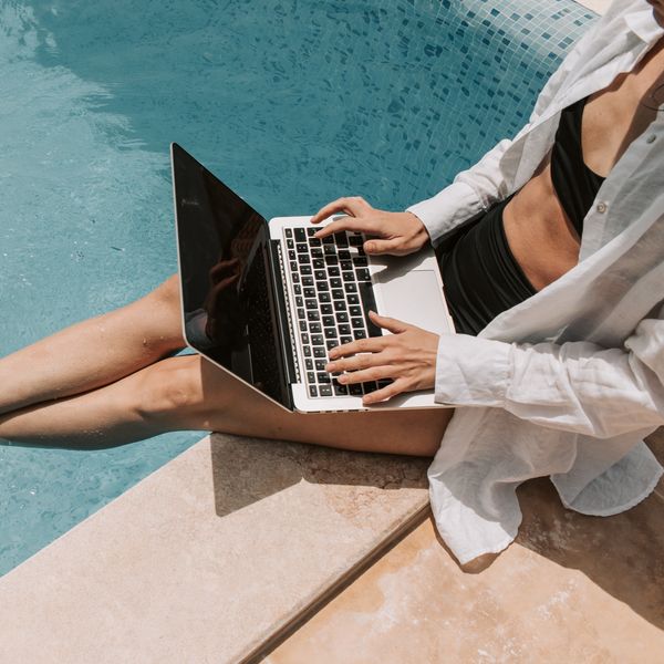woman sitting poolside using laptop on summer break