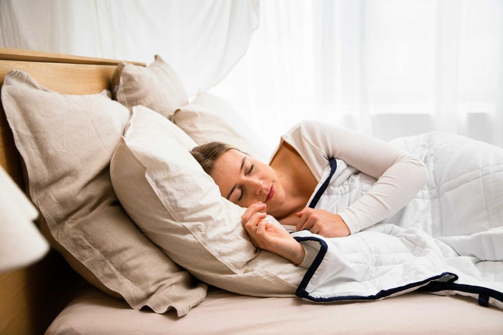 Woman sleeping in bed, cuddled under a white blanket with soft beige pillows.