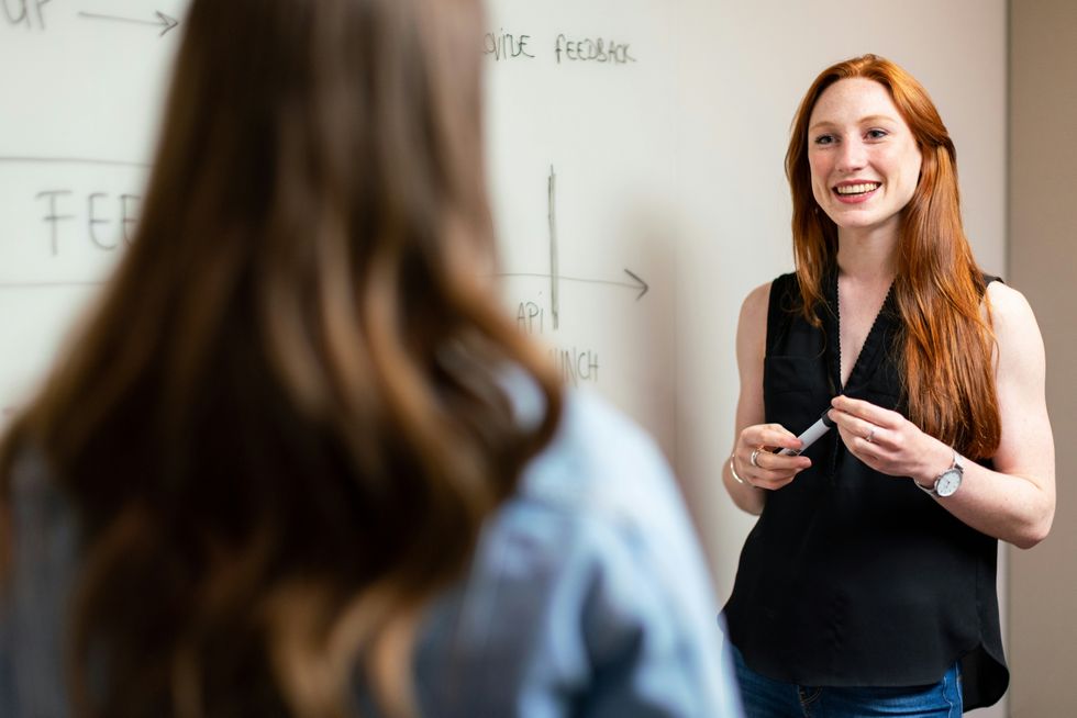 Woman smiling and presenting at a whiteboard with a marker.
