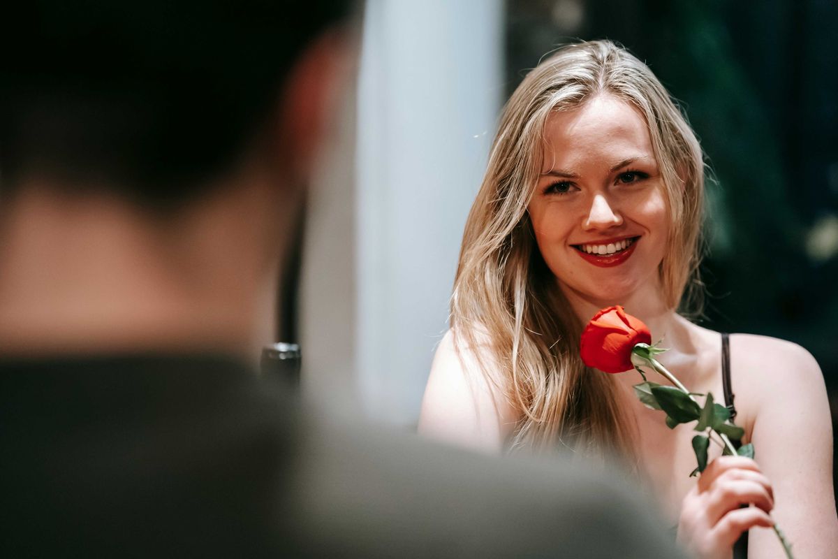 Woman smiling, holding a red rose during a romantic encounter.