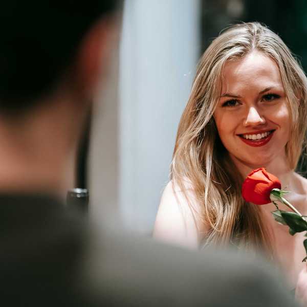 Woman smiling, holding a red rose during a romantic encounter.
