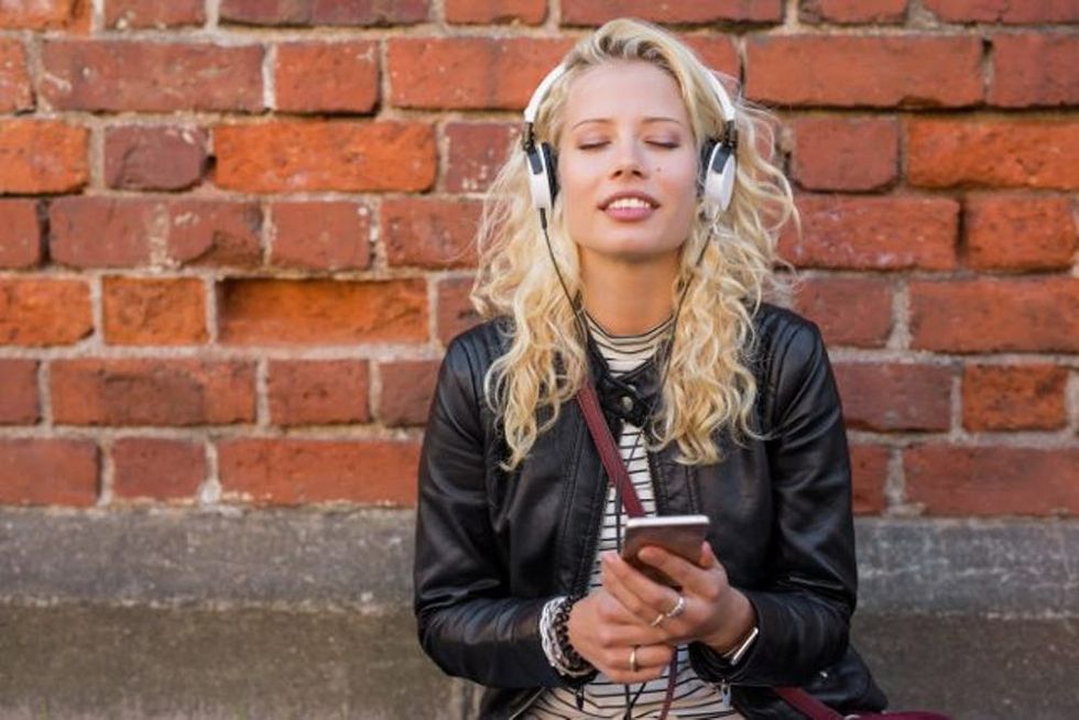 Woman stands on a street listening to headphones plugged into her phone