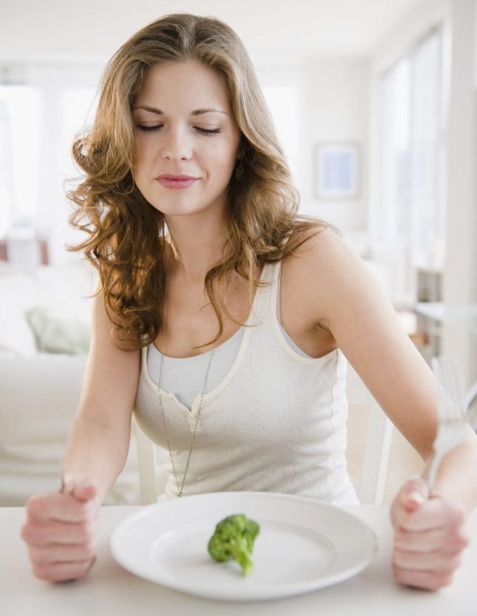 Woman staring at piece of brocolli on plate