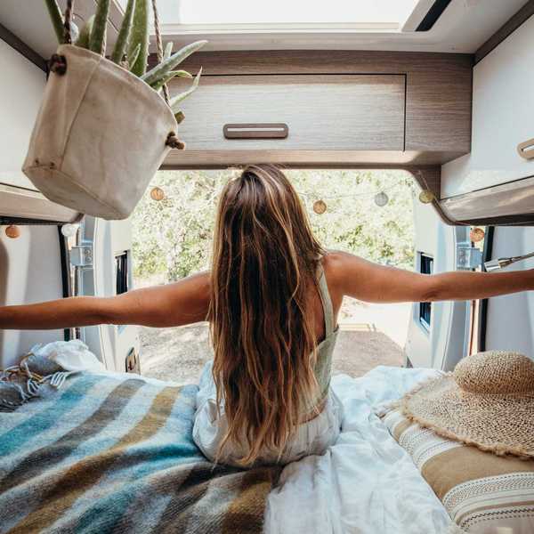 Woman stretching inside a cozy camper van with open doors to nature.
